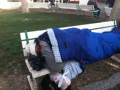 An image of a homeless man sleeping on a bench